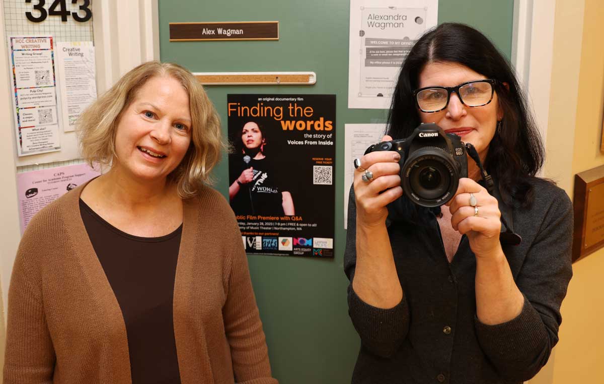 HCC English professors Lisa Mahon, left, and Alex Wagman stand next to a poster advertising the premiere of the new documentary, “Finding the Words: the story of Voices from Inside.”